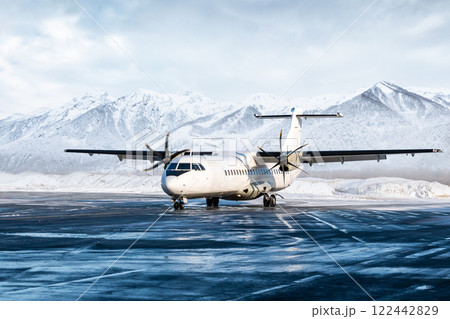 White passenger turboprop aircraft on the winter airport apron on the background of high scenic mountains 122442829