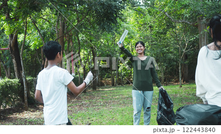 A group of dedicated young volunteers are taking part in an environmental cleaning activity in a park. Volunteers are holding big black bags. People are picking up trash and plastic bottles in a park. 122443840