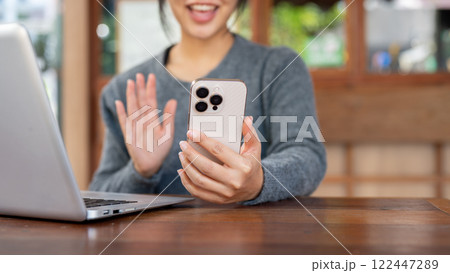 A cheerful Asian woman talks on a video call through her smartphone while sitting in a coffee shop. A cheerful Asian woman talks on a video call through her smartphone while sitting in a coffee shop. 122447289