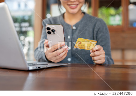 A close-up of happy Asian woman shops online on her smartphone while sitting in a cafe. A close-up of happy Asian woman shops online on her smartphone while sitting in a cafe. 122447290