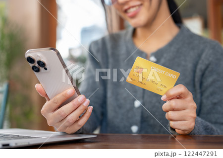 A close-up of happy Asian woman shops online on her smartphone while sitting in a cafe. 122447291