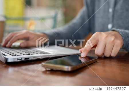 A close-up of a woman pointing at a smartphone on a table, working remotely at a coffee shop. 122447297