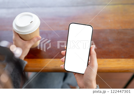 A close-up of a woman using her smartphone while sitting in a coffee shop. 122447301