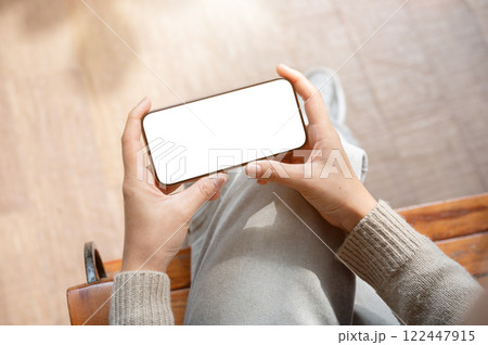 A top view of a woman sits indoors and holds her smartphone in a horizontal position. A top view of a woman sits indoors and holds her smartphone in a horizontal position. 122447915