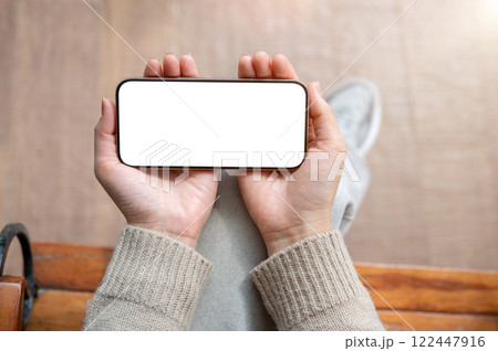 A top view of a woman sits indoors and holds her smartphone in a horizontal position. A top view of a woman sits indoors and holds her smartphone in a horizontal position. 122447916