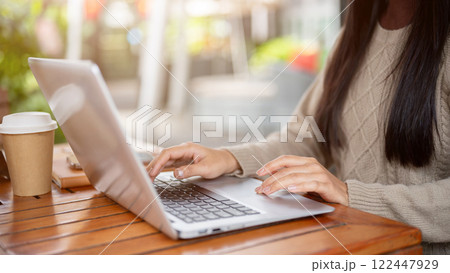 A close-up side view of a woman working on her laptop, working remotely from a cafe in the city. 122447929