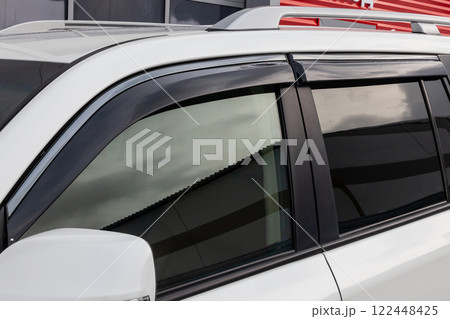 Side view of a  white Japanese car in the body of a SUV with wind visors on windows in a parking after being washed ready for sale. 122448425