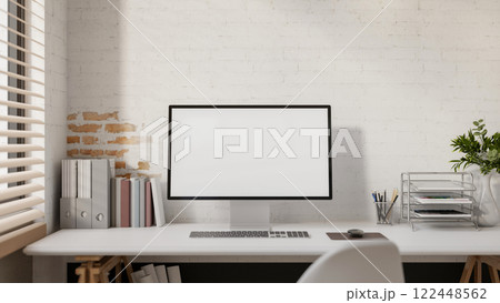 A computer and decorative items placed on a white desk against a white brick wall. 122448562