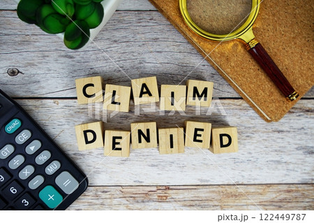 Magnifying glass and calculator with wooden blocks alphabet letters CLAIM DENIED text message on wooden background 122449787