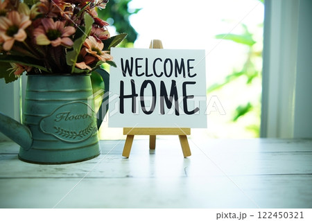 Welcome Home quotes text on paper card with easel and flowers in metal vase in the window background 122450321