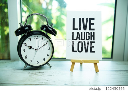 Live Laugh Love paper card with easel and alarm clock in the window background 122450363