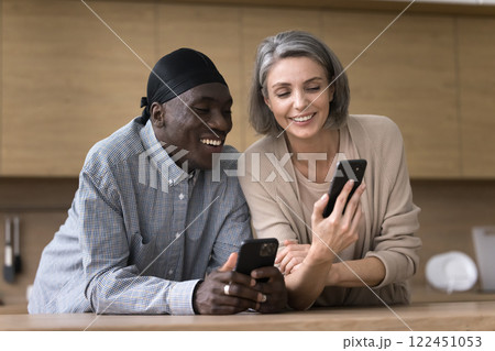 Friendly middle aged multiethnic couple share information between two smartphones Friendly middle aged multiethnic couple share information between two smartphones 122451053