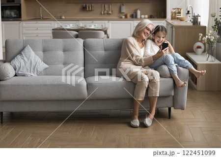 Senior grandma little granddaughter having fun on couch with phone Senior grandma little granddaughter having fun on couch with phone 122451099