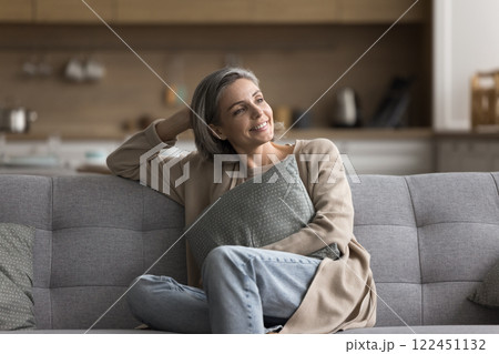 Carefree mature woman sit on sofa hug pillow look away 122451132