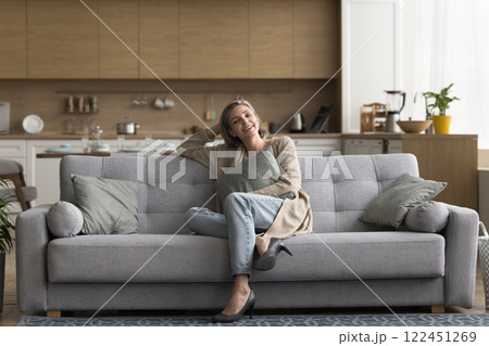 Smiling middle aged woman looking at camera sitting on sofa 122451269
