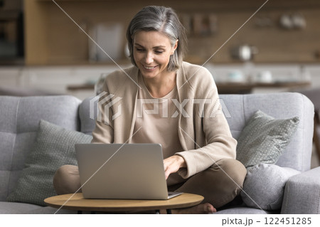 Confident aged woman working on notebook at home office remotely 122451285
