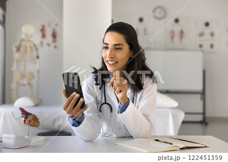 Happy woman doctor use telehealth app on phone at workplace 122451359
