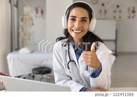Friendly doctor in headphones show thumb up gesture to camera Friendly doctor in headphones show thumb up gesture to camera 122451389