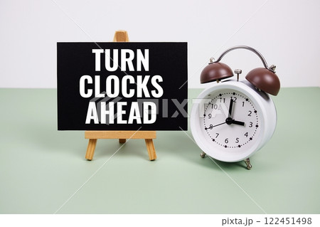 Turn Clocks Ahead text on paper card with alarm clock on green background 122451498