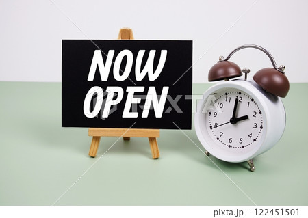 Now Open text on paper card with alarm clock on green background 122451501