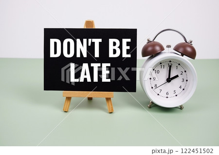 Don't Be Late text on paper card with alarm clock on green background 122451502