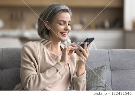 Relaxed happy mature woman interacting with phone app on couch 122451546