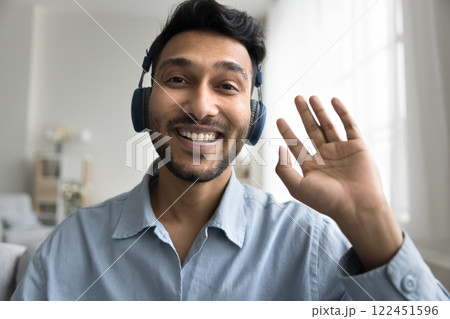 Smiling millennial male in earphones record video wave hand hi Smiling millennial male in earphones record video wave hand hi 122451596