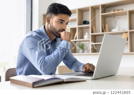 Focused reviewing data, analyzing reports using laptop 122451605