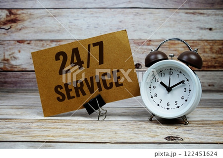 24/7 Service text on paper card with alarm clock on wooden background 122451624
