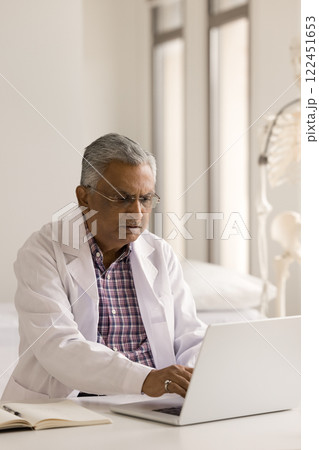 Mature man doctor type on notebook at workplace in clinic 122451653