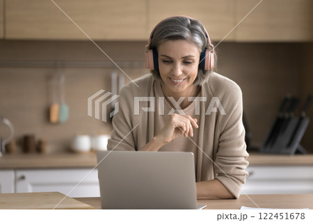 Smiling mature woman wear headset talk via videocall on notebook Smiling mature woman wear headset talk via videocall on notebook 122451678