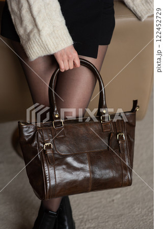 A girl in a warm sweater, a black short skirt, nylon tights, and black shoes is posing with a brown leather bag. A girl in a warm sweater, a black short skirt, nylon tights, and black shoes is posing with a brown leather bag. 122452729