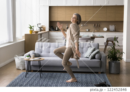 Joyful mature woman dance barefoot on carpet at cozy house Joyful mature woman dance barefoot on carpet at cozy house 122452846