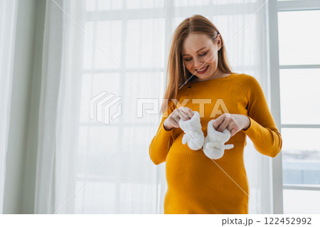 Pregnancy motherhood people expectation future. Pregnant woman with big belly holding newborn baby booties smiling at home. Young mom enjoying pregnancy. Maternity tenderness parenthood new life Pregnancy motherhood people expectation future. Pregnant woman with big belly holding newborn baby booties smiling at home. Young mom enjoying pregnancy. Maternity tenderness parenthood new life 122452992