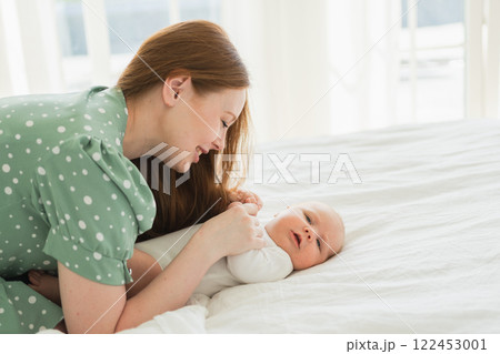 Happy family at home. Mother playing with little toddler child on bed. Mom baby relax playing having fun together. Mother looks at baby with love care. Mom of breast feeding baby rest in living room Happy family at home. Mother playing with little toddler child on bed. Mom baby relax playing having fun together. Mother looks at baby with love care. Mom of breast feeding baby rest in living room 122453001