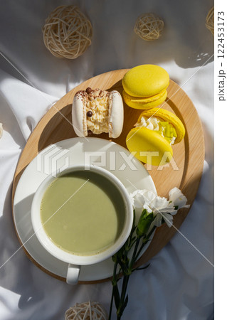 Nutrient-rich matcha drink with trendy macaron dessert on wooden tray in bed with fresh flowers. Morning beautiful breakfast present gift idea. Vibrant creative colors. Natural energy givers Nutrient-rich matcha drink with trendy macaron dessert on wooden tray in bed with fresh flowers. Morning beautiful breakfast present gift idea. Vibrant creative colors. Natural energy givers 122453173