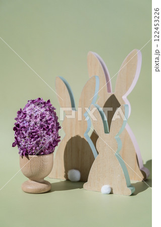 Wooden minimalism low-key bunny decor. Easter egg made of lilac spring flowers in pastel green background. Sustainable holiday minimalistic still life composition. Copy space template for invitation Wooden minimalism low-key bunny decor. Easter egg made of lilac spring flowers in pastel green background. Sustainable holiday minimalistic still life composition. Copy space template for invitation 122453226