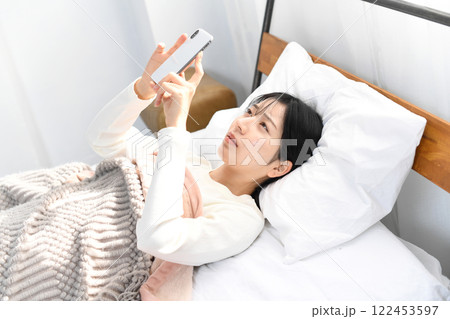 ベッドの上でスマホを持ちながら困る女性 ベッドの上でスマホを持ちながら困る女性 122453597