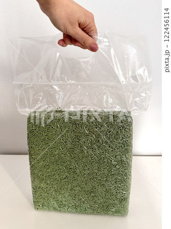 Female hand holding a transparent plastic bag with tofu litter pellets in green palette. Flushable Clumping Fast Drying Tofu Cat Ultra Absorbent Litter Pack. Premium eco litter, soluble in water. Female hand holding a transparent plastic bag with tofu litter pellets in green palette. Flushable Clumping Fast Drying Tofu Cat Ultra Absorbent Litter Pack. Premium eco litter, soluble in water. 122456114