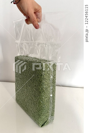 Female hand holding a transparent plastic bag with tofu litter pellets in green palette. Flushable Clumping Fast Drying Tofu Cat Ultra Absorbent Litter Pack. Premium eco litter, soluble in water. 122456115