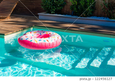 Pink donut inflatable float in turquoise swimming pool with submerged steps and wooden deck 122456127