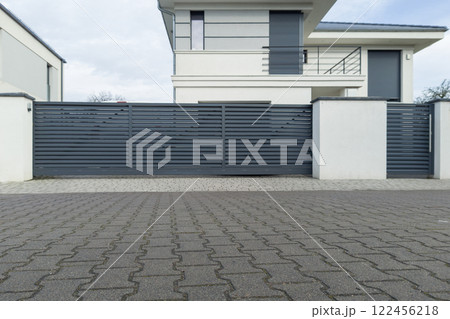 A contemporary house with a sleek sliding metal gate and a paved driveway in a residential area 122456218