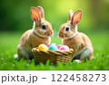 Two Easter bunnies next to basket of colorful eggs on green grass, symbols of the Christian holiday 122458273