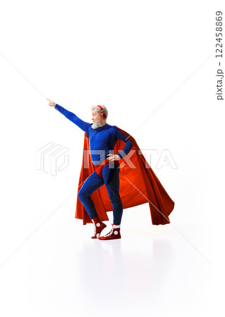 Full-length image of grey-haired man superhero costume with red cape, listening to music in headphones and raising fist up against white studio background 122458869