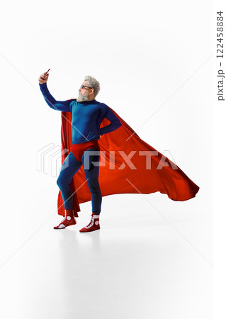 Full-length image of grey-haired young man in superhero costume standing in confident pose, in sunglasses, and taking selfie again white studio background. 122458884