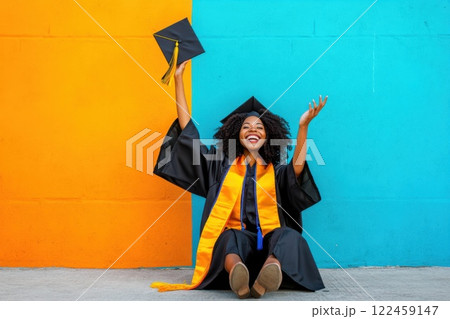 Young woman celebrates graduation with joy by tossing cap in the air against colorful backdrop 122459147
