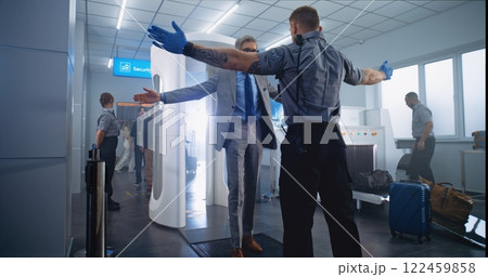 Mature Man Passes Through Metal Detector Scanner. Security Officer Checks Passenger for Plane Flight 122459858