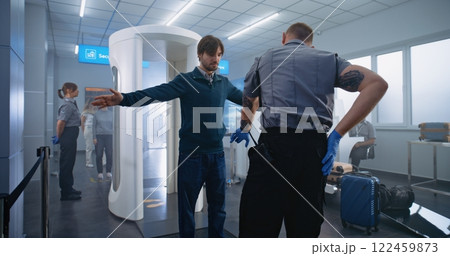 Adult Man Passes Through Metal Detector Scanner. Security Officer Checks Passenger for Plane Flight Adult Man Passes Through Metal Detector Scanner. Security Officer Checks Passenger for Plane Flight 122459873