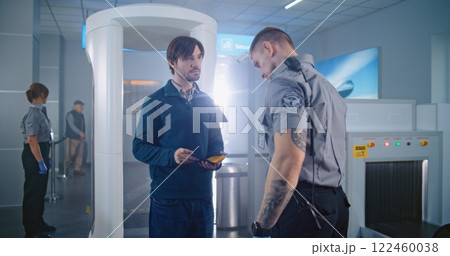 Man Passes Through Metal Detector Scanner. Security Officer Checks Documents, Inspects Passenger Man Passes Through Metal Detector Scanner. Security Officer Checks Documents, Inspects Passenger 122460038
