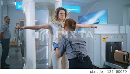 Adult Woman Walks Through Metal Detector Gates. Female Security Officer Inspects Passenger Adult Woman Walks Through Metal Detector Gates. Female Security Officer Inspects Passenger 122460079